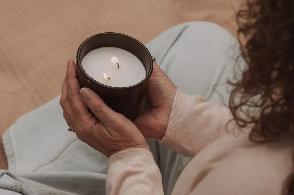 Two hands cradling a softly lit candle on the lap — warmth, ritual, calm